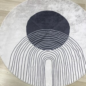 May include: A round white rug with a black and white geometric design. The design features a large circle with a series of concentric arcs and a smaller circle inside.