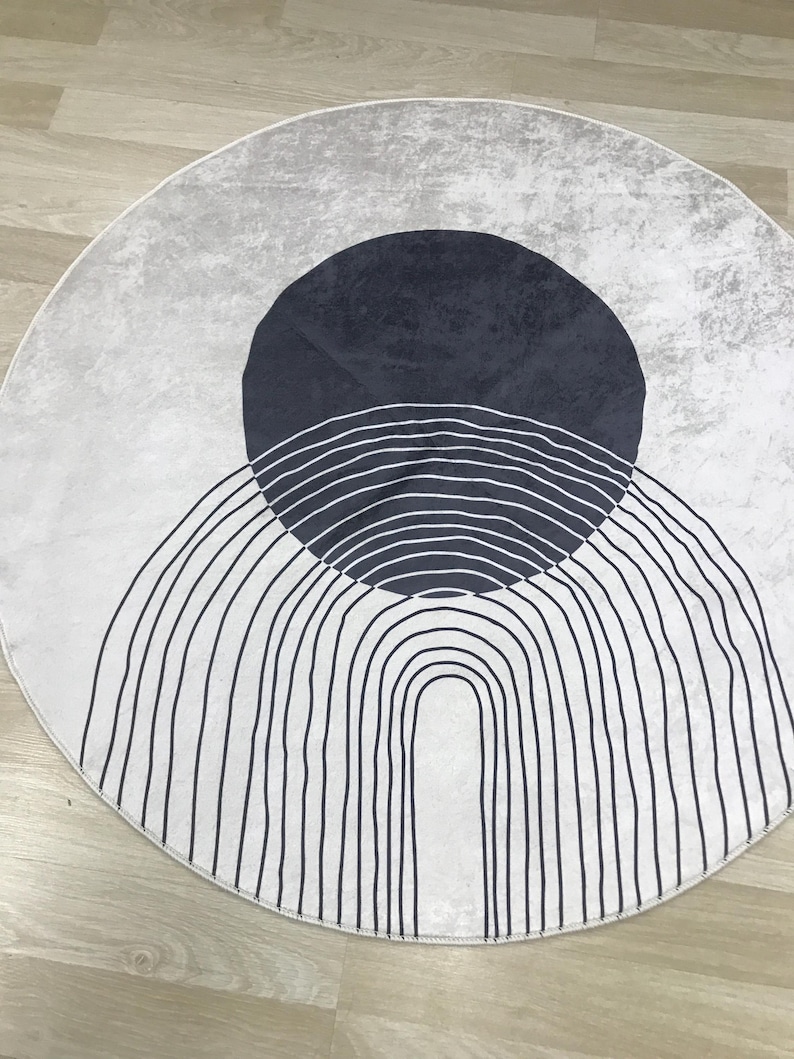 May include: A round white rug with a black and white geometric design. The design features a large circle with a series of concentric arcs and a smaller circle inside.