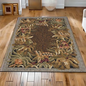 May include: Rectangular area rug with a tiger stripe pattern in the center, surrounded by a border of floral and foliage designs in shades of green, brown, and orange. The rug has a neutral-toned border.
