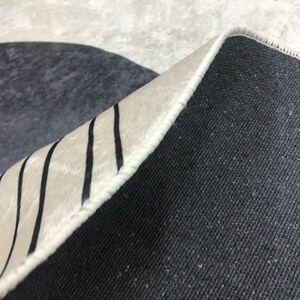 May include: Close-up of the underside of a rug with a white and black striped border. The rug has a dark gray backing.