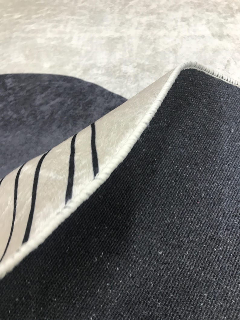 May include: Close-up of the underside of a rug with a white and black striped border. The rug has a dark gray backing.