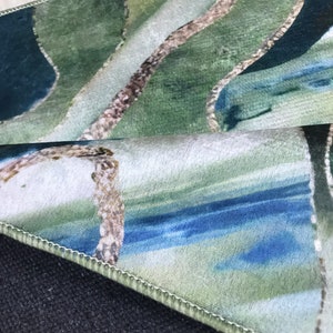 May include: Close-up of a green, blue, and white patterned rug with a stitched edge. The rug has a wavy design and is folded over on itself.