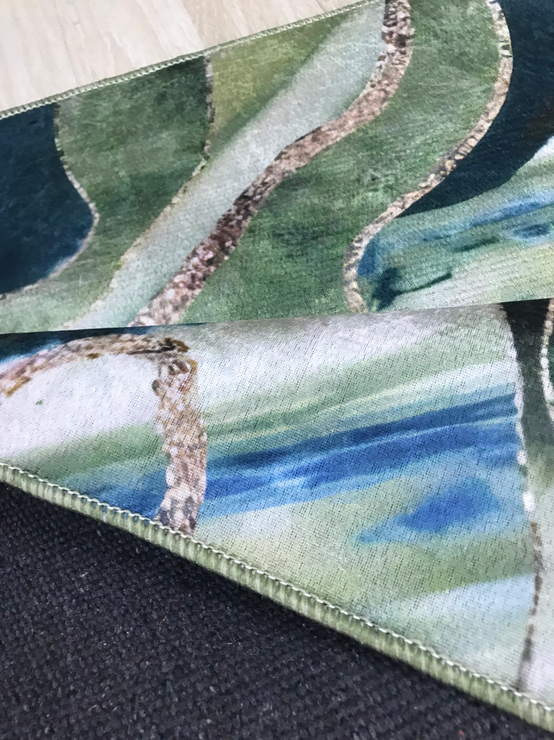 May include: Close-up of a green, blue, and white patterned rug with a stitched edge. The rug has a wavy design and is folded over on itself.
