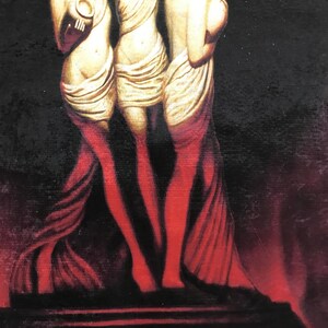 May include: Three golden statues of women standing on a red platform against a black background. The statues are wearing flowing robes and are holding up their arms.