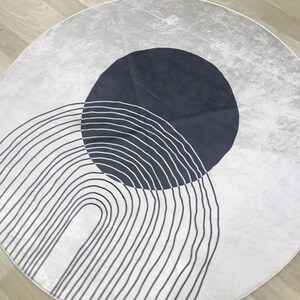 May include: A round white rug with a black and white striped arch design and a dark blue circle in the center.