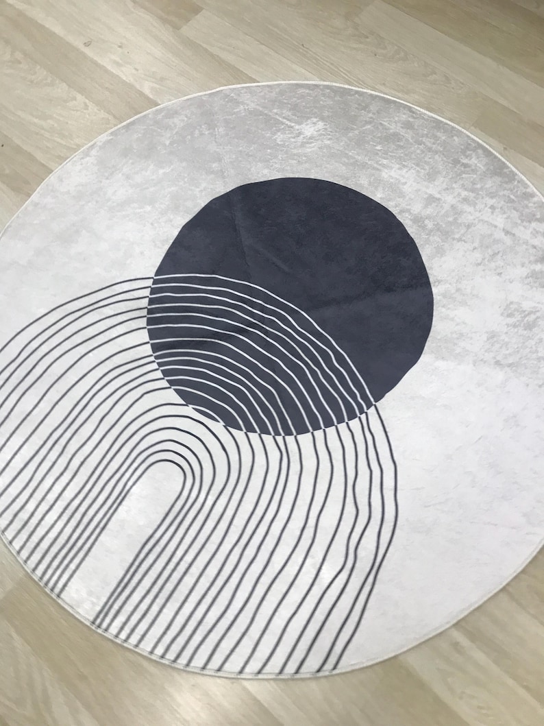 May include: A round white rug with a black and white striped arch design and a dark blue circle in the center.