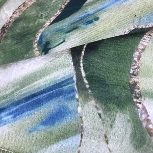 May include: Close-up of a fabric with a green, blue, and white abstract pattern. The fabric has a textured surface and a white background.