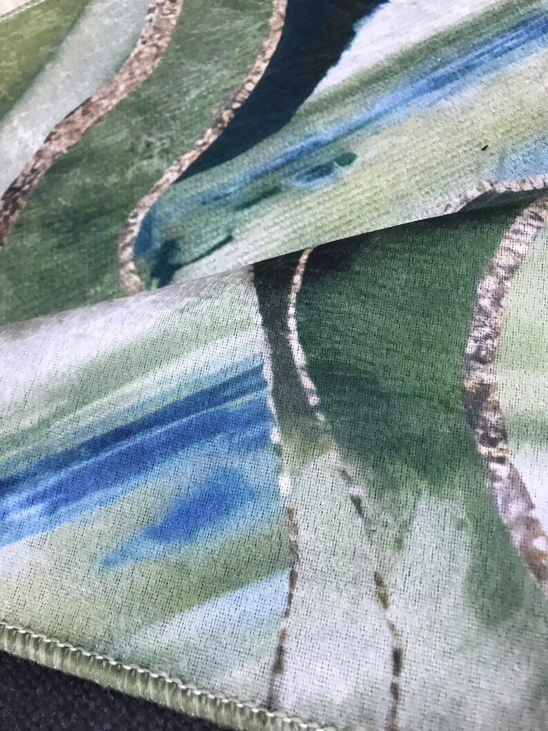 May include: Close-up of a fabric with a green, blue, and white abstract pattern. The fabric has a textured surface and a white background.