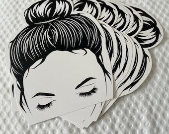 May include: A stack of white paper cutouts with a black silhouette of a woman with her hair in a bun. The woman's eyes are closed and she has eyelashes.