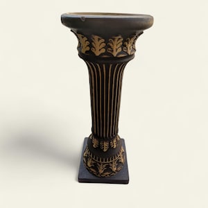 May include: A dark brown decorative column with gold leaf detailing. The column has a square base and a fluted shaft. The top of the column is bowl-shaped. The column is a decorative item, possibly for display.