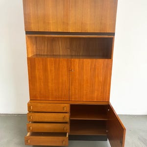 Puede incluir: Un mueble alto de madera de estilo moderno de mediados de siglo con un acabado marr&oacute;n rojizo c&aacute;lido. Cuenta con armarios superiores, estanter&iacute;as abiertas, un armario inferior con puerta y cuatro cajones. El dise&ntilde;o del mueble incluye una banda negra y una base negra.