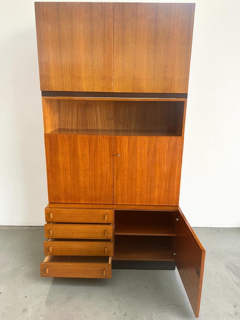Puede incluir: Un mueble alto de madera de estilo moderno de mediados de siglo con un acabado marr&oacute;n rojizo c&aacute;lido. Cuenta con armarios superiores, estanter&iacute;as abiertas, un armario inferior con puerta y cuatro cajones. El dise&ntilde;o del mueble incluye una banda negra y una base negra.