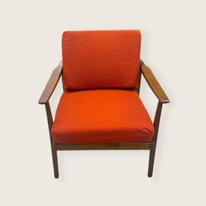 May include: Mid-century modern armchair with a vibrant orange textured fabric seat and back. The chair features a wooden frame and armrests, showcasing a classic design. The chair's dimensions are approximately 30 inches wide, 30 inches deep, and 30 inches high.