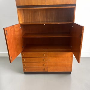 Puede incluir: Un mueble de madera de estilo moderno de mediados de siglo con puertas abiertas, que revelan estantes y cajones. El mueble es de madera marr&oacute;n claro con una base y molduras marr&oacute;n oscuro. Las puertas est&aacute;n abiertas.