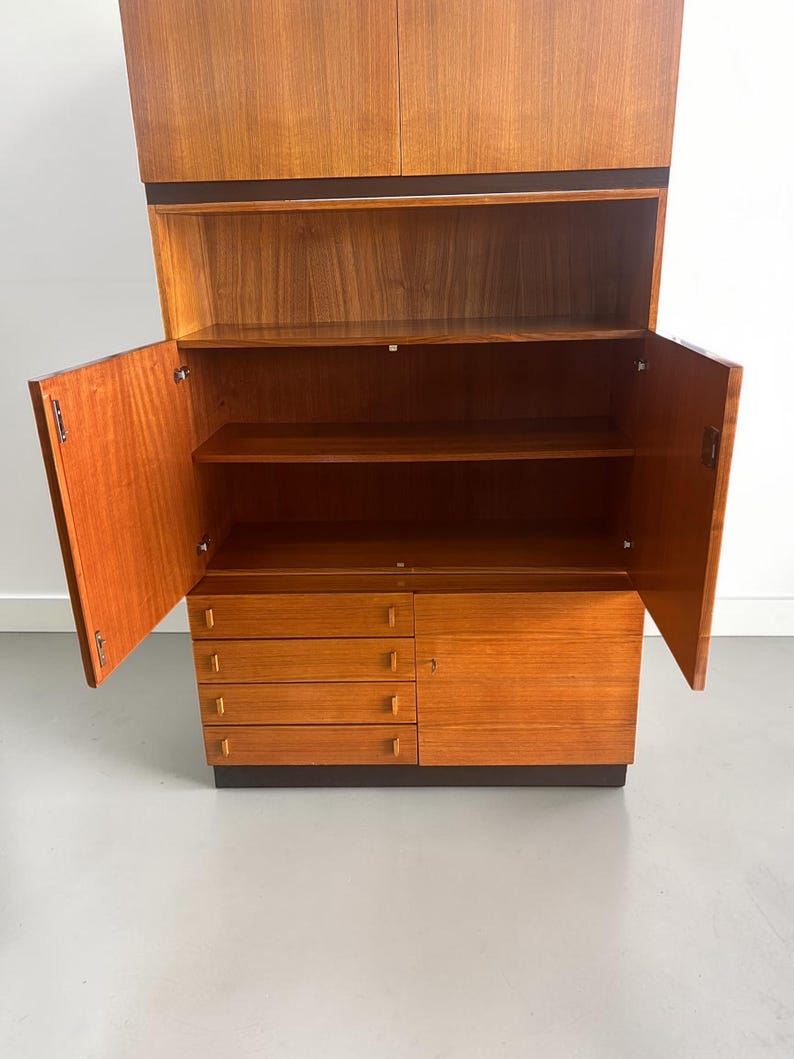 Puede incluir: Un mueble de madera de estilo moderno de mediados de siglo con puertas abiertas, que revelan estantes y cajones. El mueble es de madera marr&oacute;n claro con una base y molduras marr&oacute;n oscuro. Las puertas est&aacute;n abiertas.