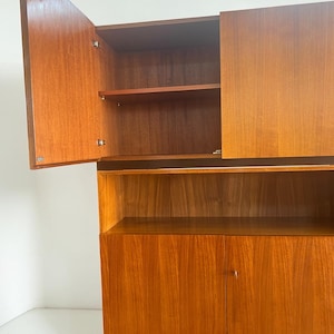 Puede incluir: Un mueble de madera con un acabado marr&oacute;n rojizo c&aacute;lido. El mueble tiene dos puertas en la parte inferior, un estante en el medio y dos puertas en la parte superior, una de las cuales est&aacute; abierta. Los estantes interiores son visibles.