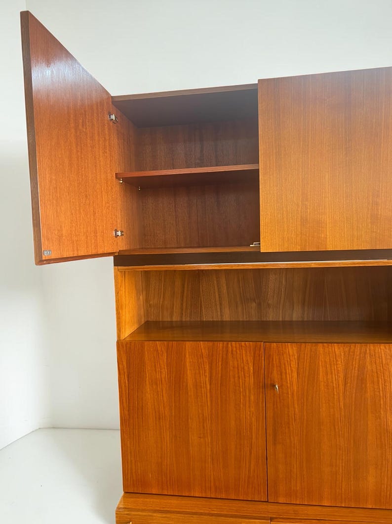 Puede incluir: Un mueble de madera con un acabado marr&oacute;n rojizo c&aacute;lido. El mueble tiene dos puertas en la parte inferior, un estante en el medio y dos puertas en la parte superior, una de las cuales est&aacute; abierta. Los estantes interiores son visibles.