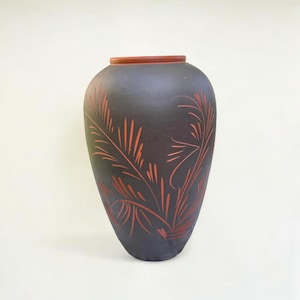 Peut inclure: Un vase en céramique gris foncé avec un corps large et un col étroit. Le vase présente un motif botanique orange rougeâtre. Le bord du vase est de couleur brun rougeâtre. Le vase est un objet décoratif.