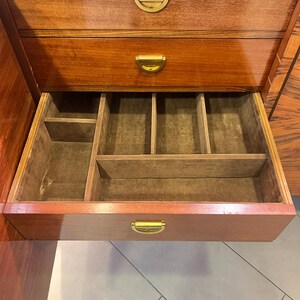 May include: A wooden cabinet with three drawers. The top two drawers have brass handles. The bottom drawer is open and has a felt-lined interior with compartments.
