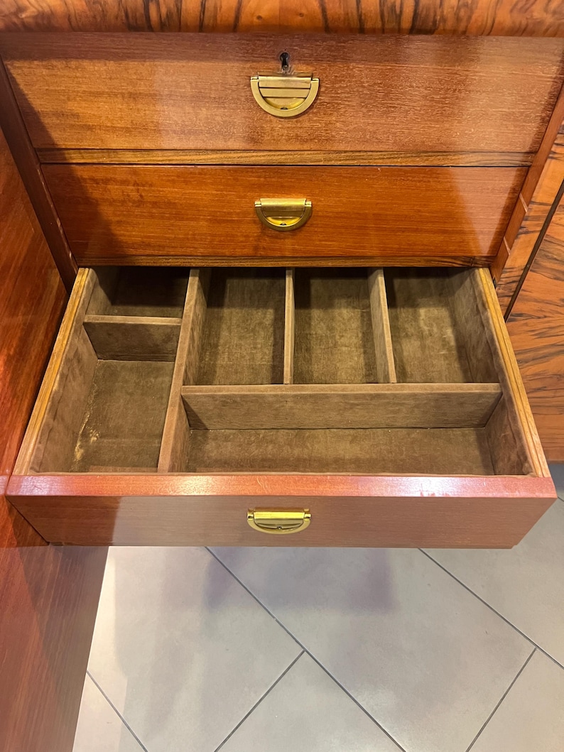 May include: A wooden cabinet with three drawers. The top two drawers have brass handles. The bottom drawer is open and has a felt-lined interior with compartments.