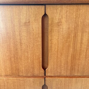 Puede incluir: Un armario de madera con dos puertas y un dise&ntilde;o de manija &uacute;nico recortado. El armario tiene un acabado de madera marr&oacute;n claro.