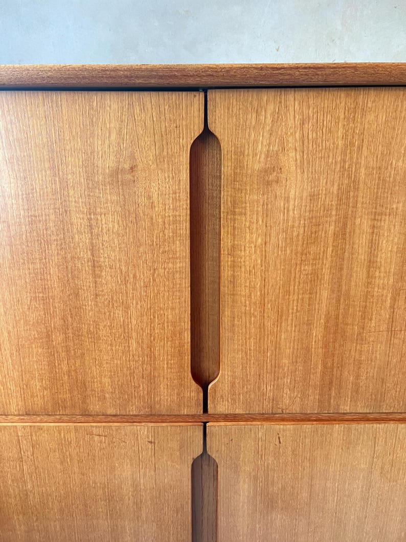 Puede incluir: Un armario de madera con dos puertas y un dise&ntilde;o de manija &uacute;nico recortado. El armario tiene un acabado de madera marr&oacute;n claro.