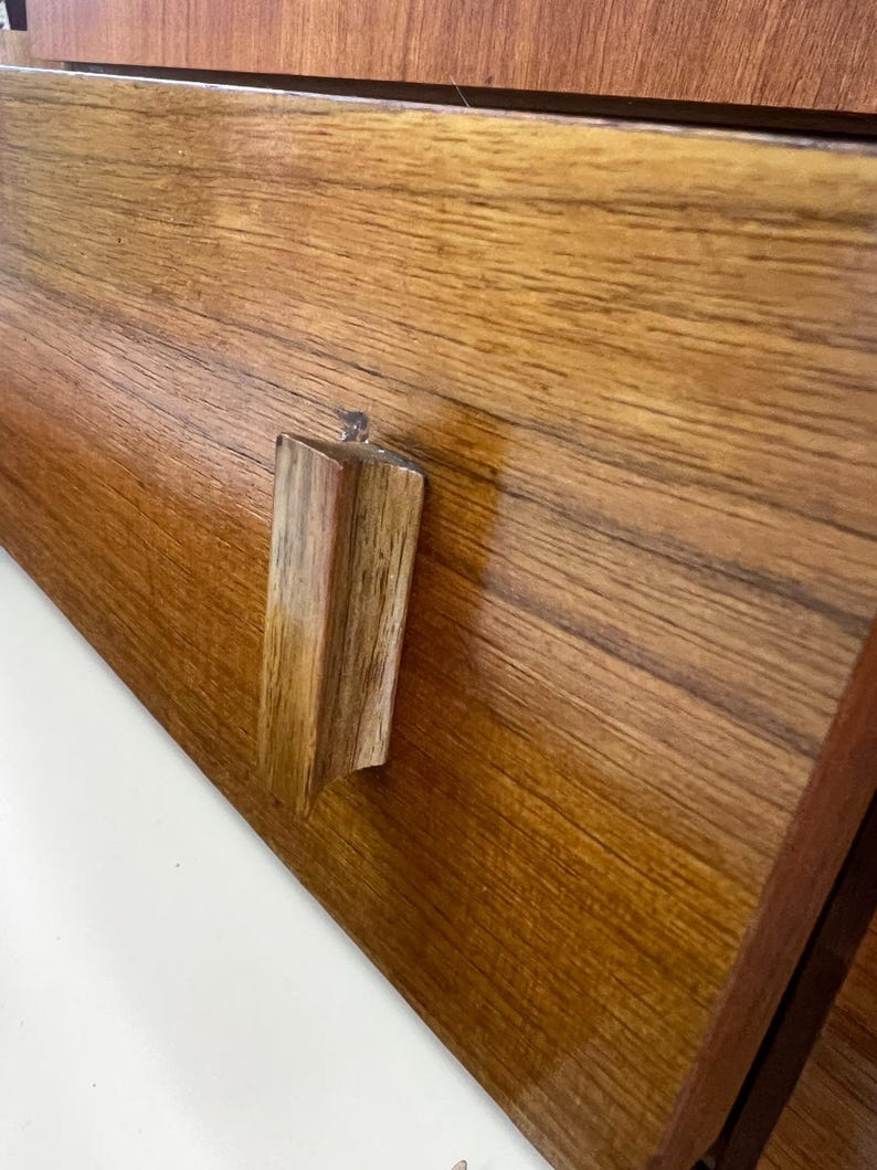 Puede incluir: Primer plano de un caj&oacute;n de madera con un tirador rectangular de madera. El caj&oacute;n es de madera marr&oacute;n claro con vetas visibles. El tirador es de un tono m&aacute;s claro y tiene un accesorio transparente similar al pl&aacute;stico.