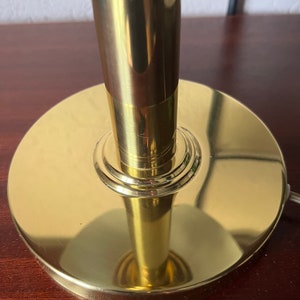 Puede incluir: Primer plano de una base y un v&aacute;stago de l&aacute;mpara dorados. La base es un disco circular ancho con un acabado pulido. El v&aacute;stago es cil&iacute;ndrico y tambi&eacute;n tiene un aspecto dorado brillante. La l&aacute;mpara parece ser de metal.