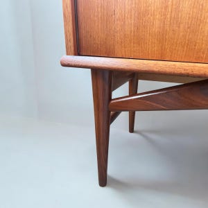 Puede incluir: Primer plano de la parte inferior de un armario de madera con un acabado marr&oacute;n claro. El armario tiene cuatro patas que son anguladas y c&oacute;nicas. Las patas est&aacute;n hechas de madera maciza y tienen un acabado natural.