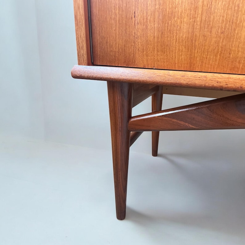 Puede incluir: Primer plano de la parte inferior de un armario de madera con un acabado marr&oacute;n claro. El armario tiene cuatro patas que son anguladas y c&oacute;nicas. Las patas est&aacute;n hechas de madera maciza y tienen un acabado natural.