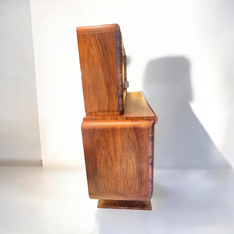 May include: A vintage wooden cabinet with a curved design and a glass-front top section. The cabinet is made of rich, dark wood with a natural grain pattern.