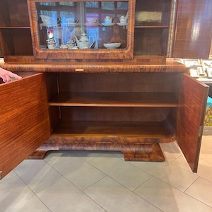 May include: A vintage wooden cabinet with glass doors and shelves. The cabinet has a dark wood finish and intricate details. The doors are open, revealing the interior shelves.