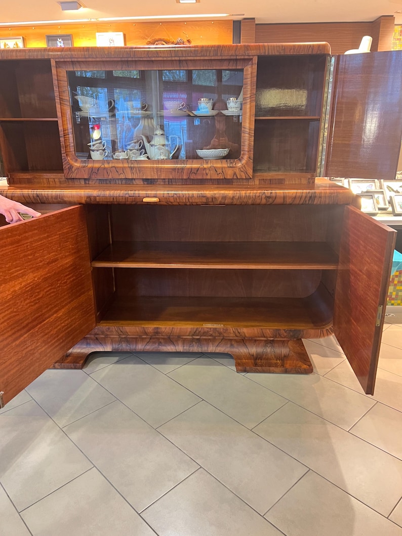 May include: A vintage wooden cabinet with glass doors and shelves. The cabinet has a dark wood finish and intricate details. The doors are open, revealing the interior shelves.