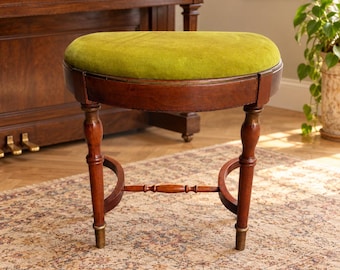 Puede incluir: Un taburete redondo de madera con un asiento tapizado en terciopelo verde lima vibrante. La base está construida en madera oscura pulida con cuatro patas torneadas, un travesaño central de soporte y casquillos de latón.