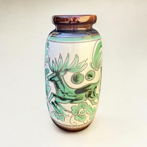 May include: A ceramic vase with a brown rim and base, and a white body. The vase is decorated with a green deer and floral design. The deer is leaping, and the flowers are stylized. The vase has a glossy finish.