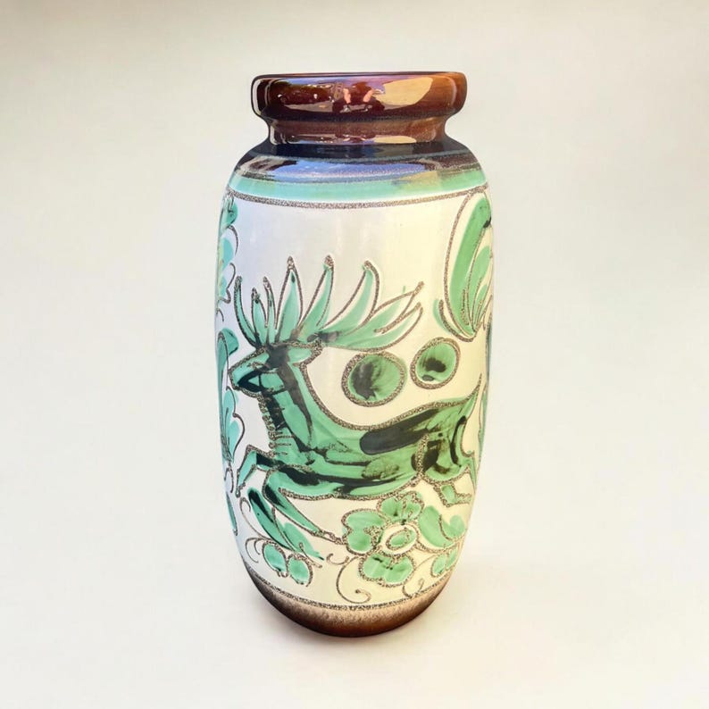 May include: A ceramic vase with a brown rim and base, and a white body. The vase is decorated with a green deer and floral design. The deer is leaping, and the flowers are stylized. The vase has a glossy finish.