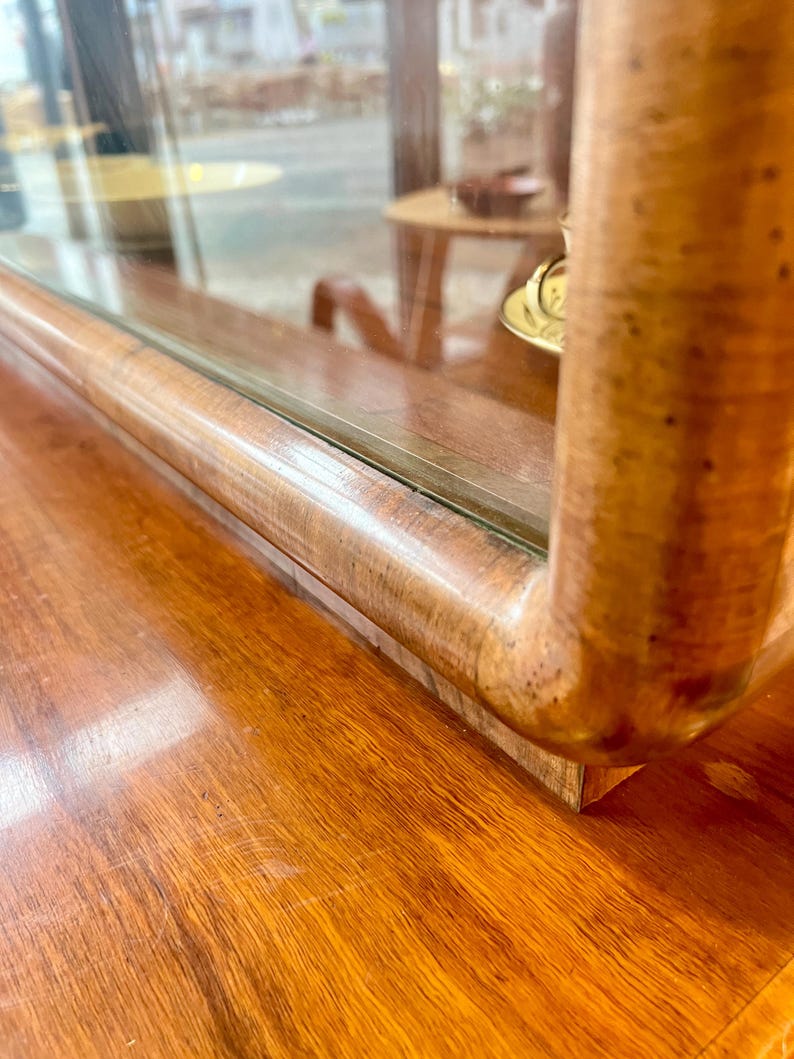 May include: Close-up of the top edge of a wooden cabinet with a glass display case. The cabinet has a rich brown wood finish and the glass is clear. The wood has a natural grain pattern.