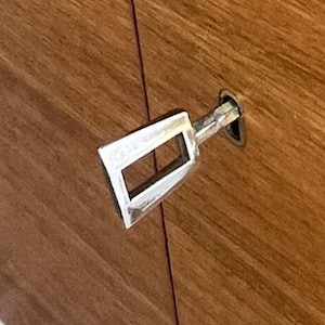 Puede incluir: Una llave plateada insertada en un armario de madera. La llave tiene una abertura rectangular y se encuentra sobre un fondo de vetas de madera marr&oacute;n c&aacute;lido. La llave est&aacute; en &aacute;ngulo, lo que sugiere que est&aacute; en uso.