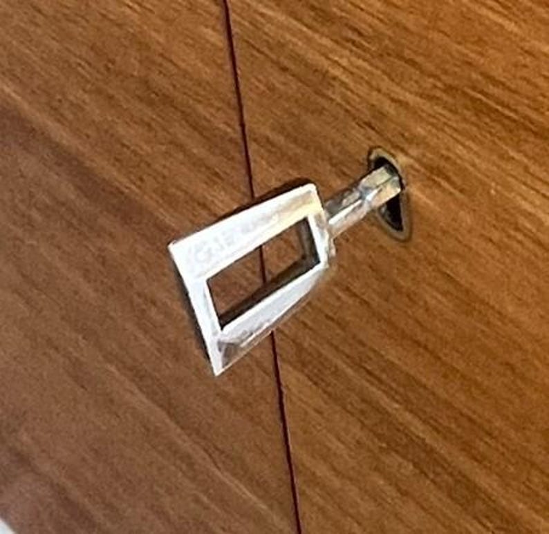 Puede incluir: Una llave plateada insertada en un armario de madera. La llave tiene una abertura rectangular y se encuentra sobre un fondo de vetas de madera marr&oacute;n c&aacute;lido. La llave est&aacute; en &aacute;ngulo, lo que sugiere que est&aacute; en uso.