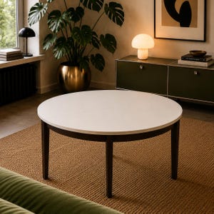 Könnte beinhalten: Ein runder Couchtisch mit einer glatten, weißen, kreisförmigen Tischplatte, die von vier dunkelbraunen Holzbeinen getragen wird. Der Tisch hat ein schlichtes Design mit einer sichtbaren Naht in der Mitte der Platte, die auf eine Ausziehfunktion hindeutet.