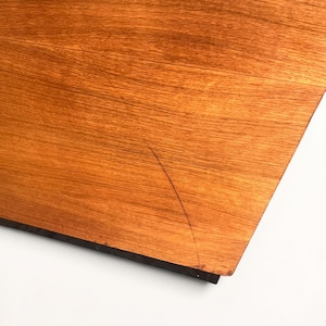 Puede incluir: Primer plano de una secci&oacute;n de una superficie de madera con un tono c&aacute;lido marr&oacute;n rojizo. La veta de la madera es visible y hay un borde oscuro. Una fina grieta es visible en la superficie.