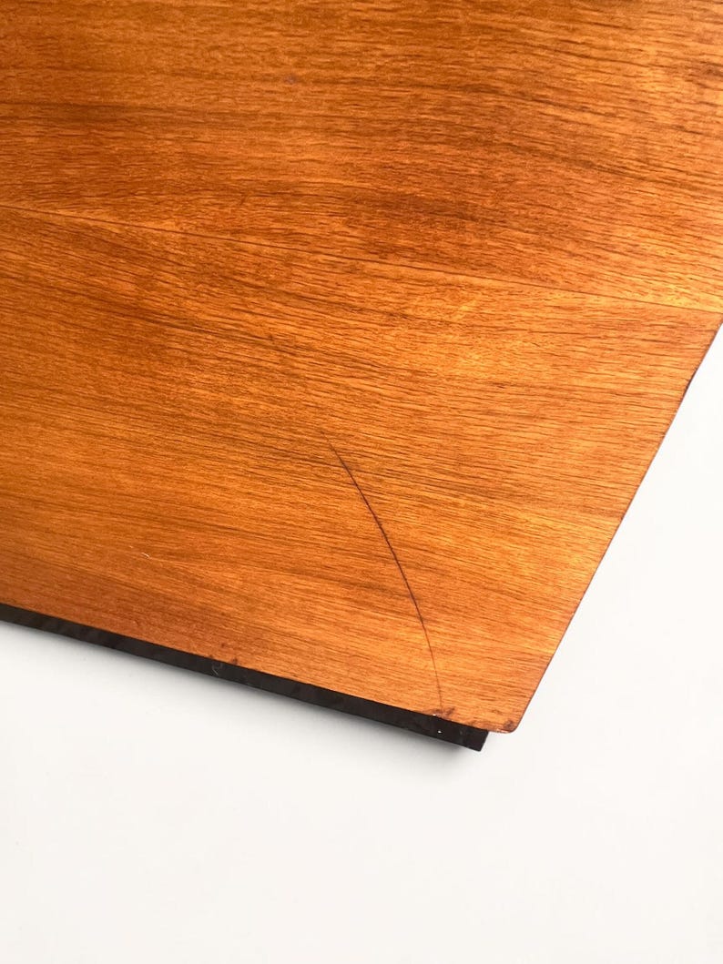 Puede incluir: Primer plano de una secci&oacute;n de una superficie de madera con un tono c&aacute;lido marr&oacute;n rojizo. La veta de la madera es visible y hay un borde oscuro. Una fina grieta es visible en la superficie.