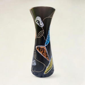 Könnte beinhalten: Eine schwarze Keramikvase mit ausgestelltem Oberteil und schmalem Boden. Die Vase ist mit farbenfrohen abstrakten Formen in Weiß, Blau, Orange und Gelb verziert. Das Design zeigt eine Mischung aus geometrischen und organischen Formen.