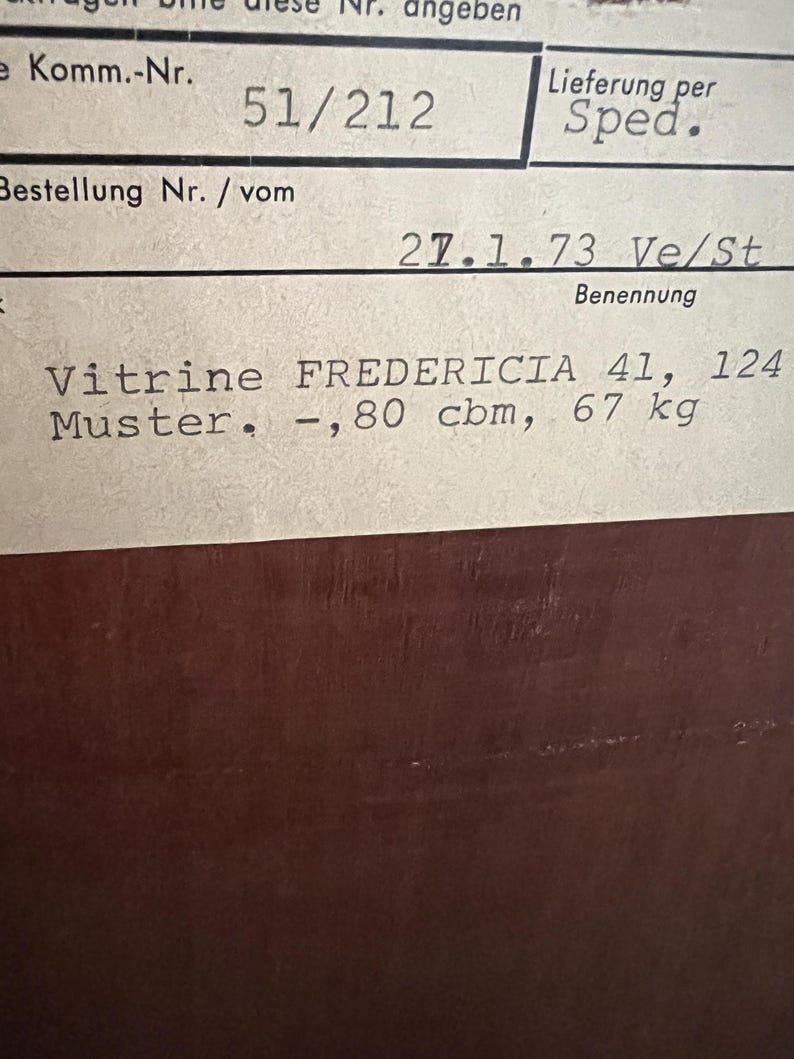 Puede incluir: Un primer plano de una etiqueta blanca con texto negro. La etiqueta dice "Komm.-Nr. 51/212", "Bestellung Nr. / vom 27.1.73 Ve/St", "Benennung", "Vitrine FREDERICIA 41, 124", "Muster. -,80 cbm, 67 kg".