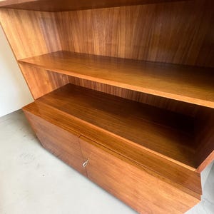 Puede incluir: Una estanter&iacute;a de madera con m&uacute;ltiples estantes y un armario. La estanter&iacute;a est&aacute; hecha de madera marr&oacute;n claro con vetas naturales. Los estantes son abiertos y el armario tiene una puerta con un tirador plateado. El dise&ntilde;o es moderno y geom&eacute;trico.