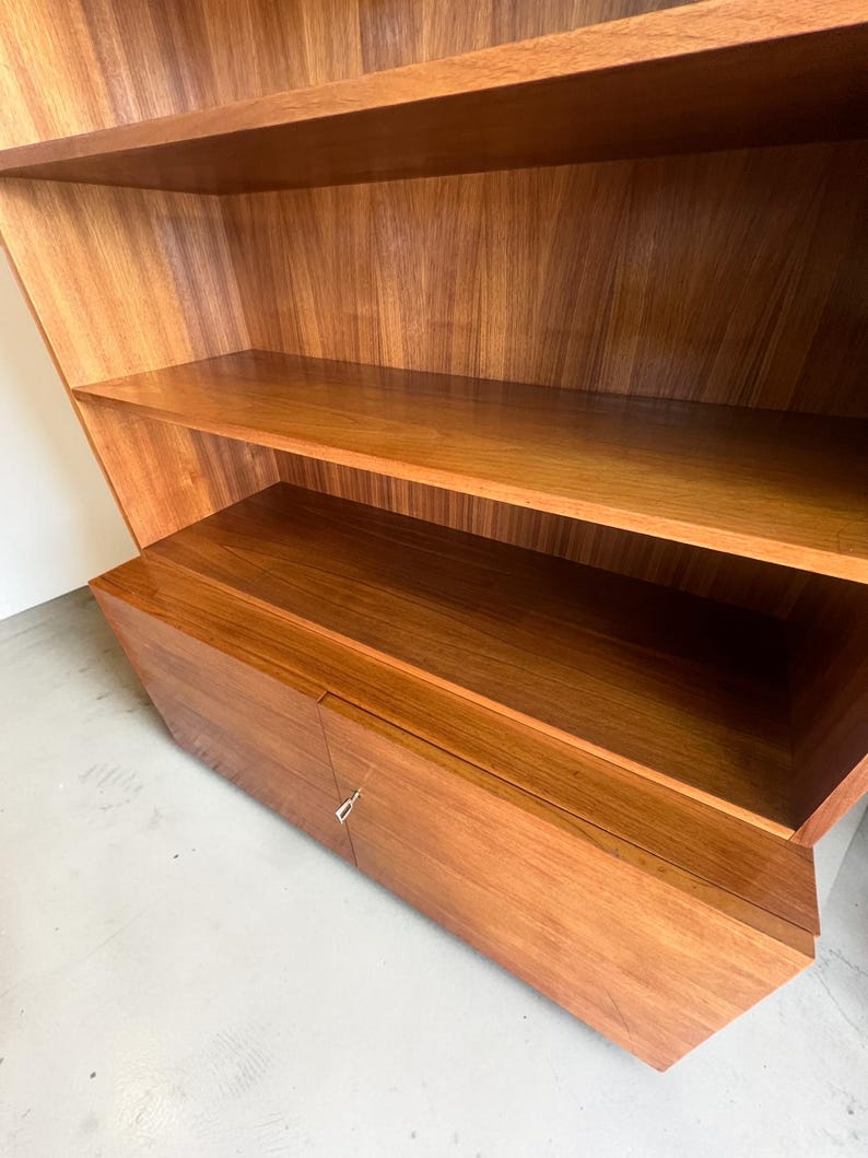 Puede incluir: Una estanter&iacute;a de madera con m&uacute;ltiples estantes y un armario. La estanter&iacute;a est&aacute; hecha de madera marr&oacute;n claro con vetas naturales. Los estantes son abiertos y el armario tiene una puerta con un tirador plateado. El dise&ntilde;o es moderno y geom&eacute;trico.