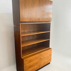 Puede incluir: Un mueble alto de madera de estilo moderno de mediados de siglo con un acabado marr&oacute;n claro. El mueble cuenta con una secci&oacute;n superior con dos puertas, estanter&iacute;as abiertas en el medio y una secci&oacute;n inferior con dos puertas. El mueble est&aacute; sobre una base marr&oacute;n oscuro.