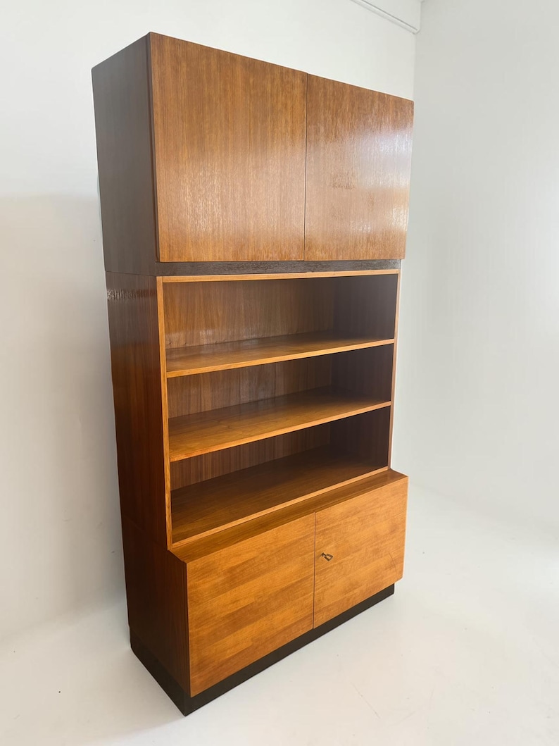 Puede incluir: Un mueble alto de madera de estilo moderno de mediados de siglo con un acabado marr&oacute;n claro. El mueble cuenta con una secci&oacute;n superior con dos puertas, estanter&iacute;as abiertas en el medio y una secci&oacute;n inferior con dos puertas. El mueble est&aacute; sobre una base marr&oacute;n oscuro.