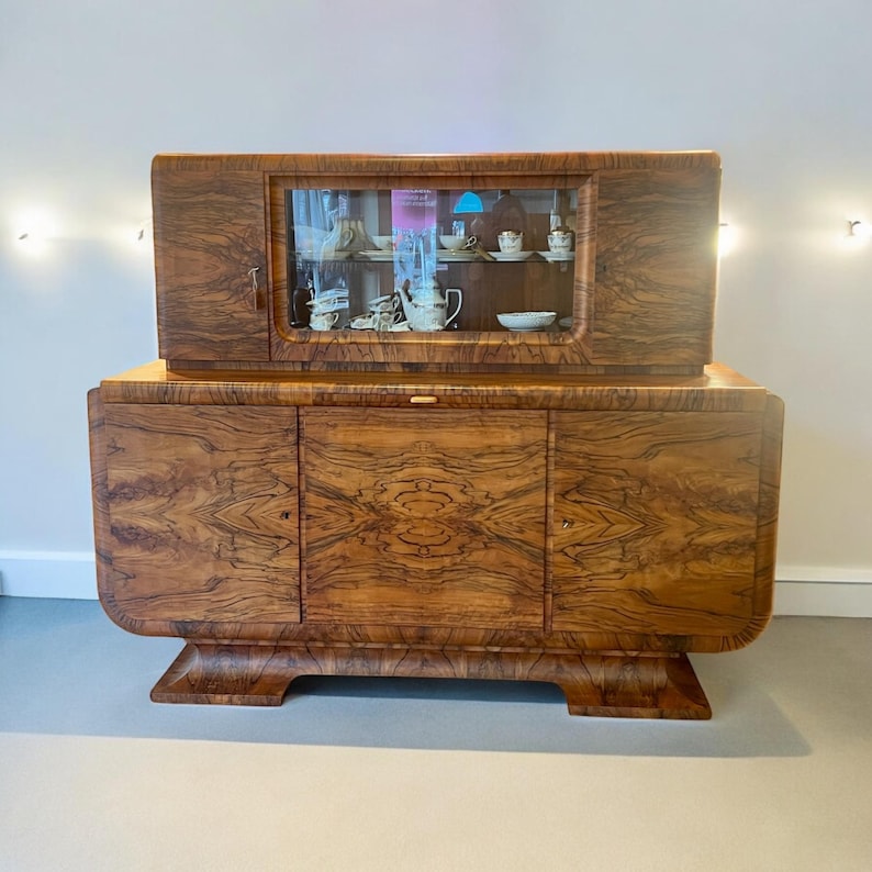 May include: A vintage wooden cabinet with a glass-front top section and three doors on the bottom. The cabinet has a rich brown wood grain and features curved legs.