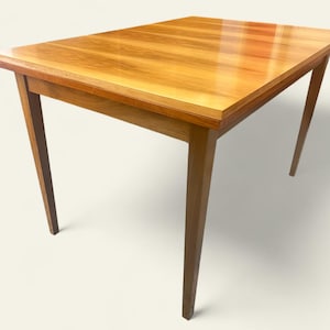 May include: A rectangular wooden table with a glossy finish. The table has a light brown colour and four angled legs. The table is likely used for dining or as a desk. The table's dimensions are approximately 120 cm x 80 cm.